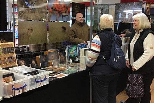 two ladies chatting with Ashley Vincent at his picture display stand at Kempton Park Racecourse
